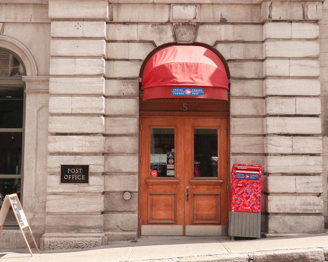 A red telephone booth on a brown brick wall representing a post office location