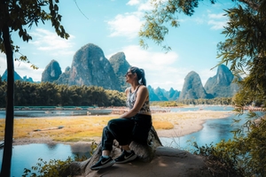 Femme sur un rocher avec les montagnes de Guilin en arrière-plan.
