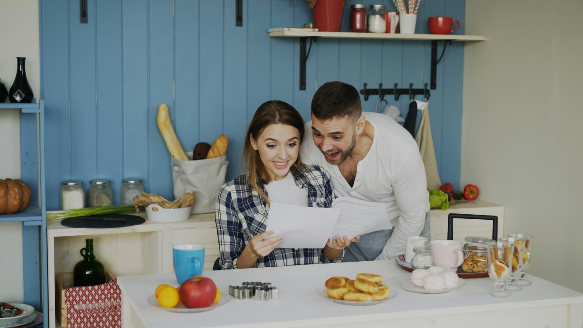 Un couple ravi de recevoir une carte postale dans une cuisine lumineuse