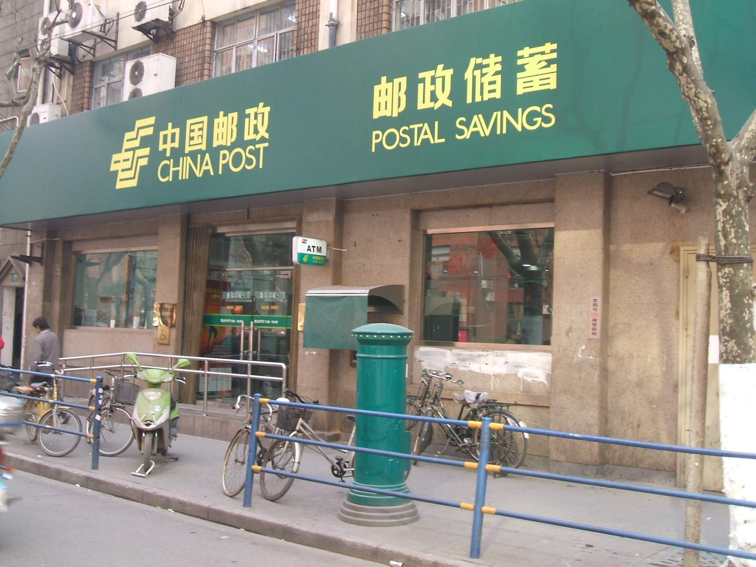 Außenansicht einer China Post Filiale in Shanghai mit grünem Logo und Schriftzeichen.
