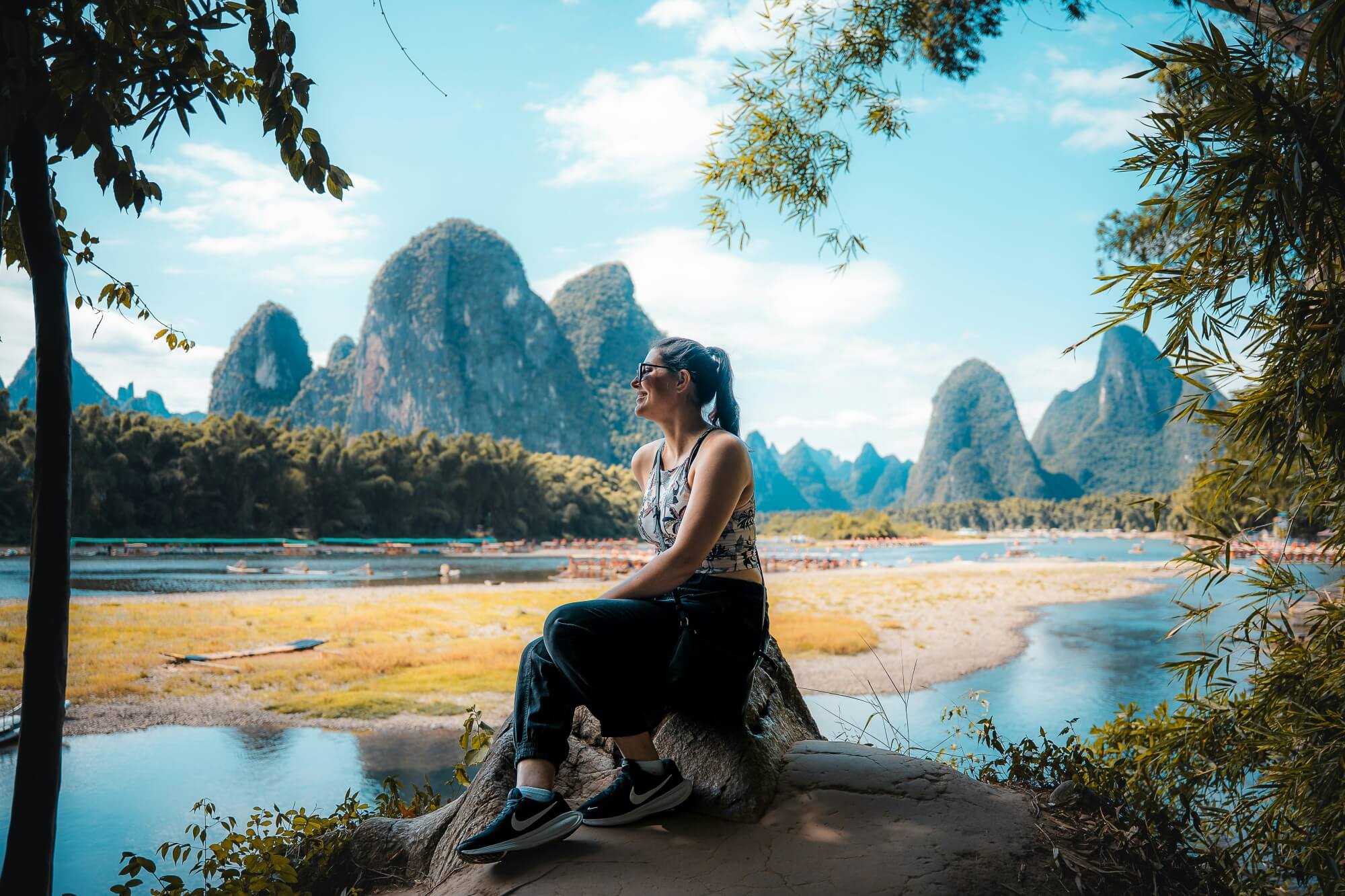 Frau sitzt auf einem Felsen mit den Karstbergen von Guilin im Hintergrund.
