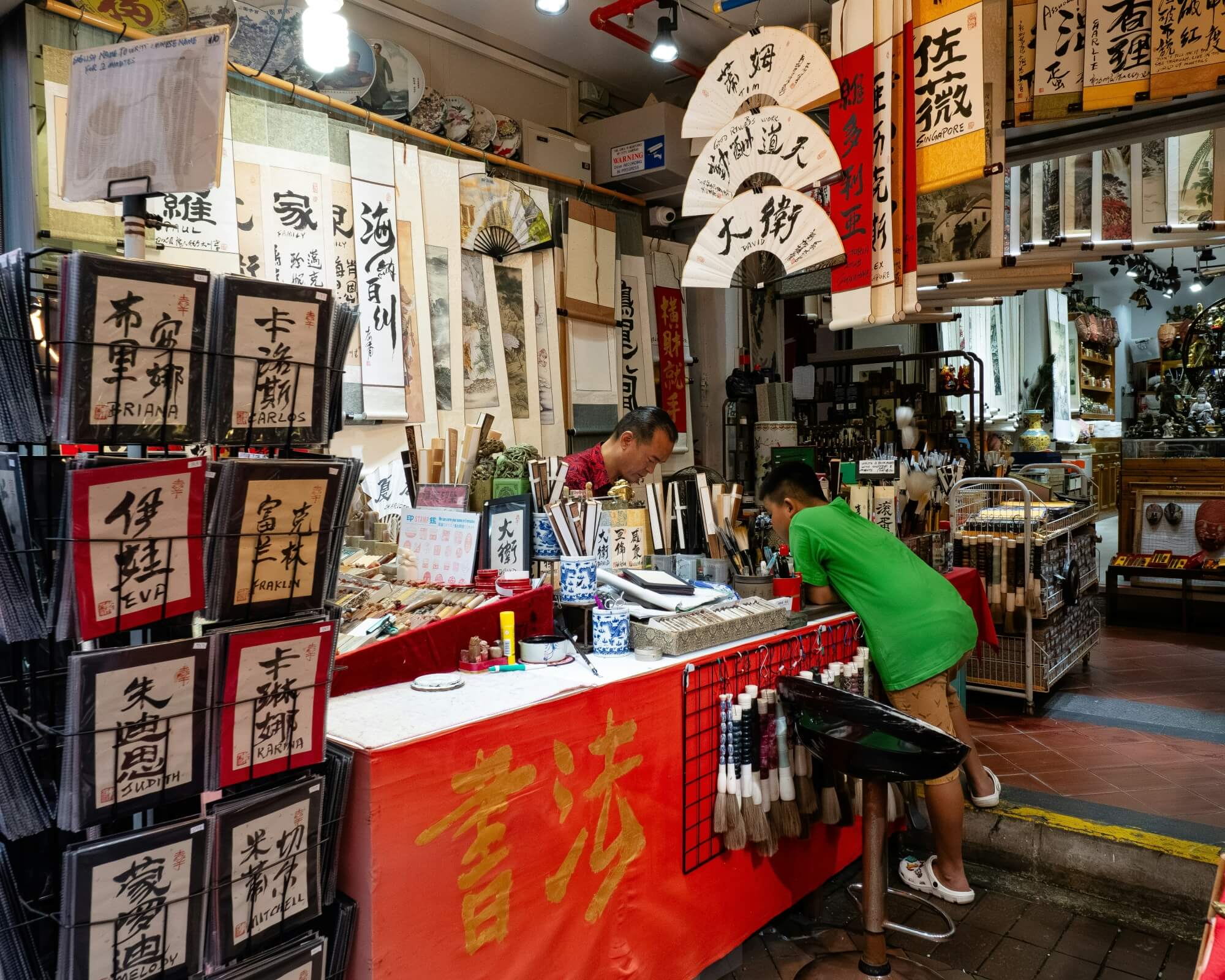 Mann sitzt an einem Verkaufsstand in einem chinesischen Laden – typische Einkaufssituation für Postkarten und Briefmarken.