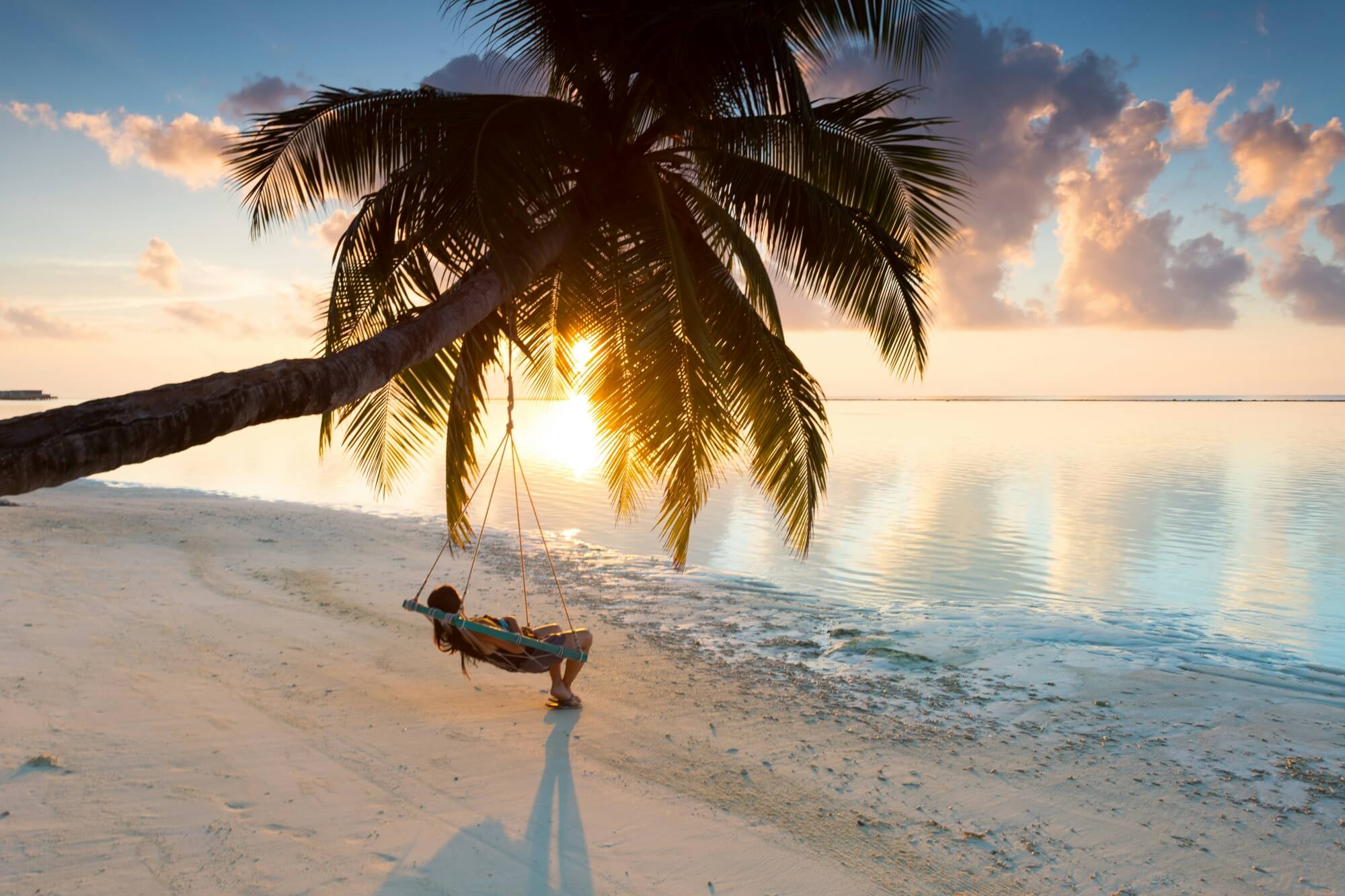 Eine Frau genießt den Sonnenuntergang in einer Hängematte am Strand.