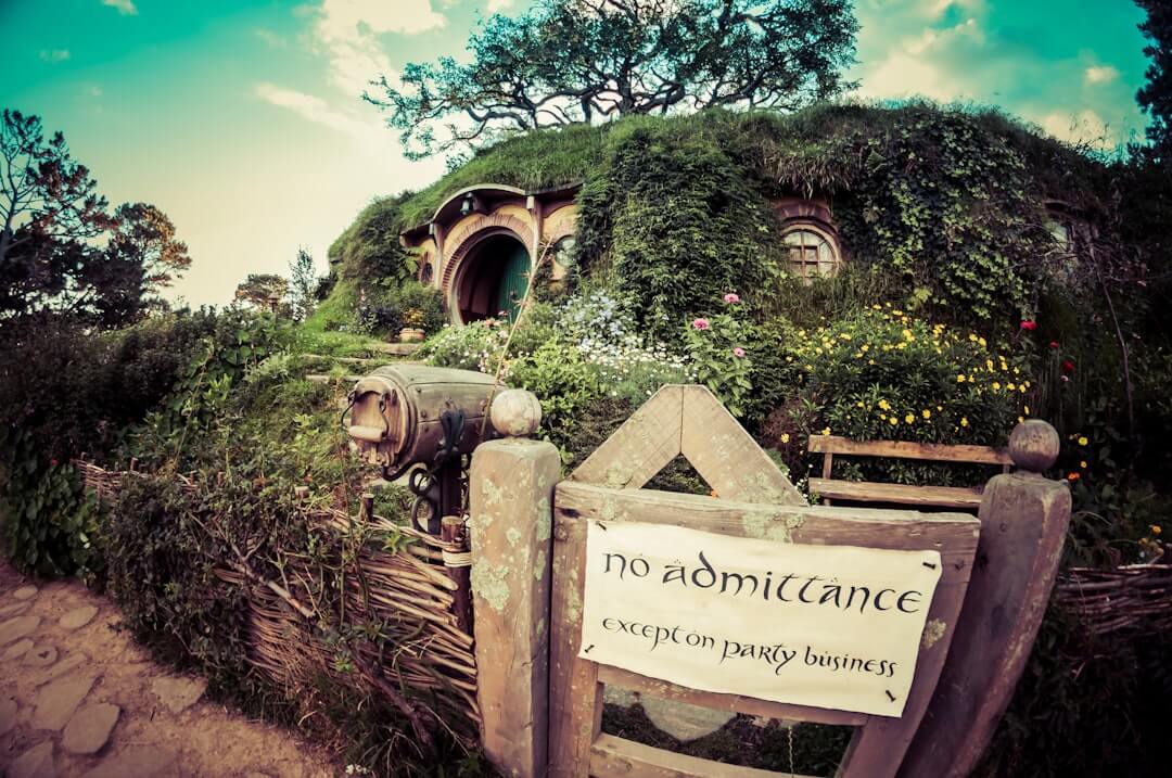 Grünes Hobbit-Haus mit runder Tür inmitten einer malerischen Wiese in Hobbiton, Neuseeland.
