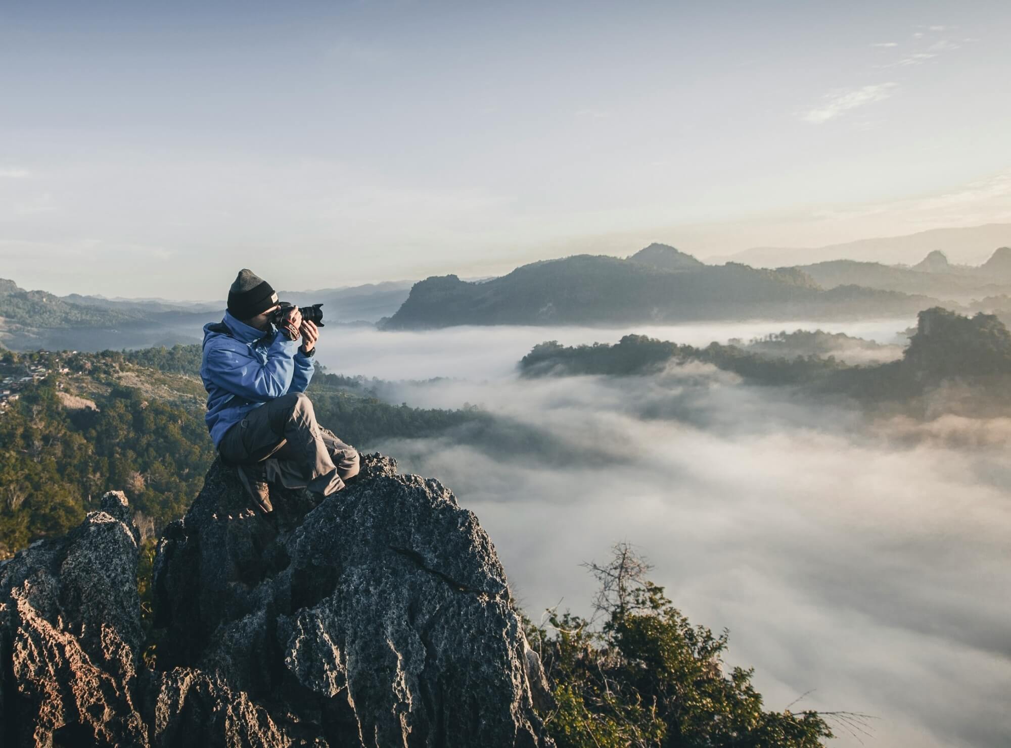 Eine Person in den Bergen hält eine Kamera in der Hand und fotografiert ein Postkartenmotiv.